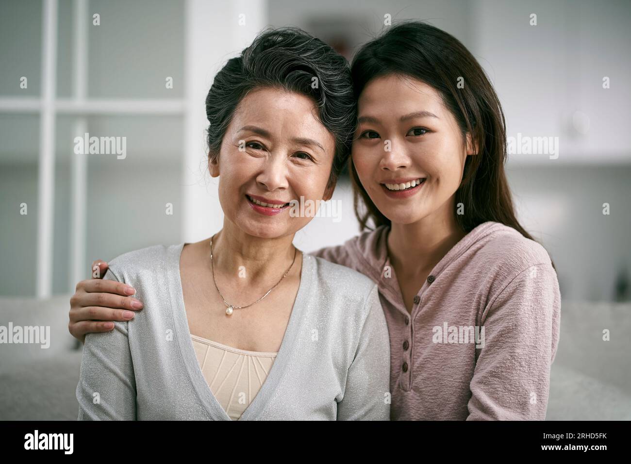 Porträt einer asiatischen älteren Mutter und erwachsenen Tochter, die zu Hause glücklich und lächelnd auf der Couch sitzt Stockfoto