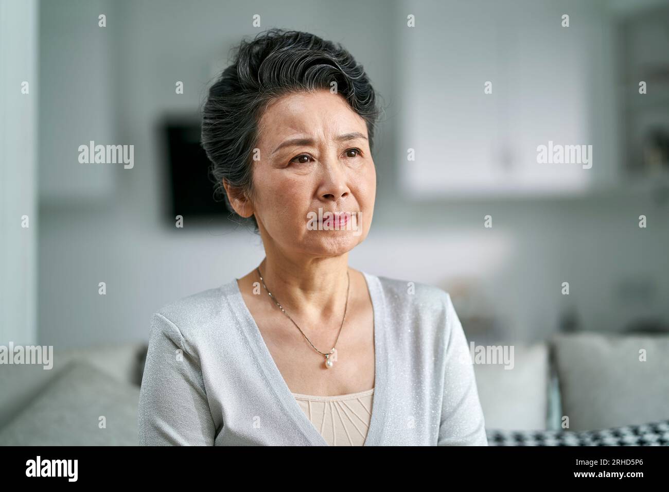 Porträt einer unglücklichen älteren asiatischen Frau, die zu Hause auf der Couch sitzt Stockfoto