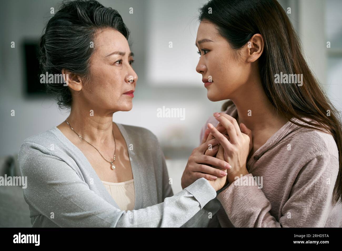 Junge asiatische Erwachsenentochter tröstet Seniormutter mit psychischer Erkrankung Stockfoto