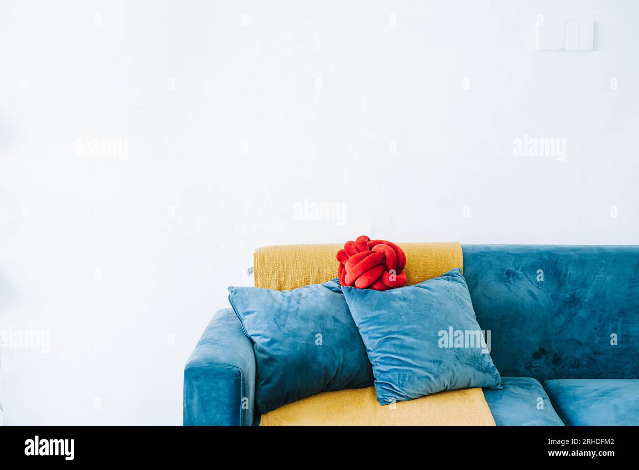 Blaues Sofa, 2 massive Kissen und ein rotes Kissen mit goldenem Überwurf vor weißer Wand als Hintergrund Stockfoto