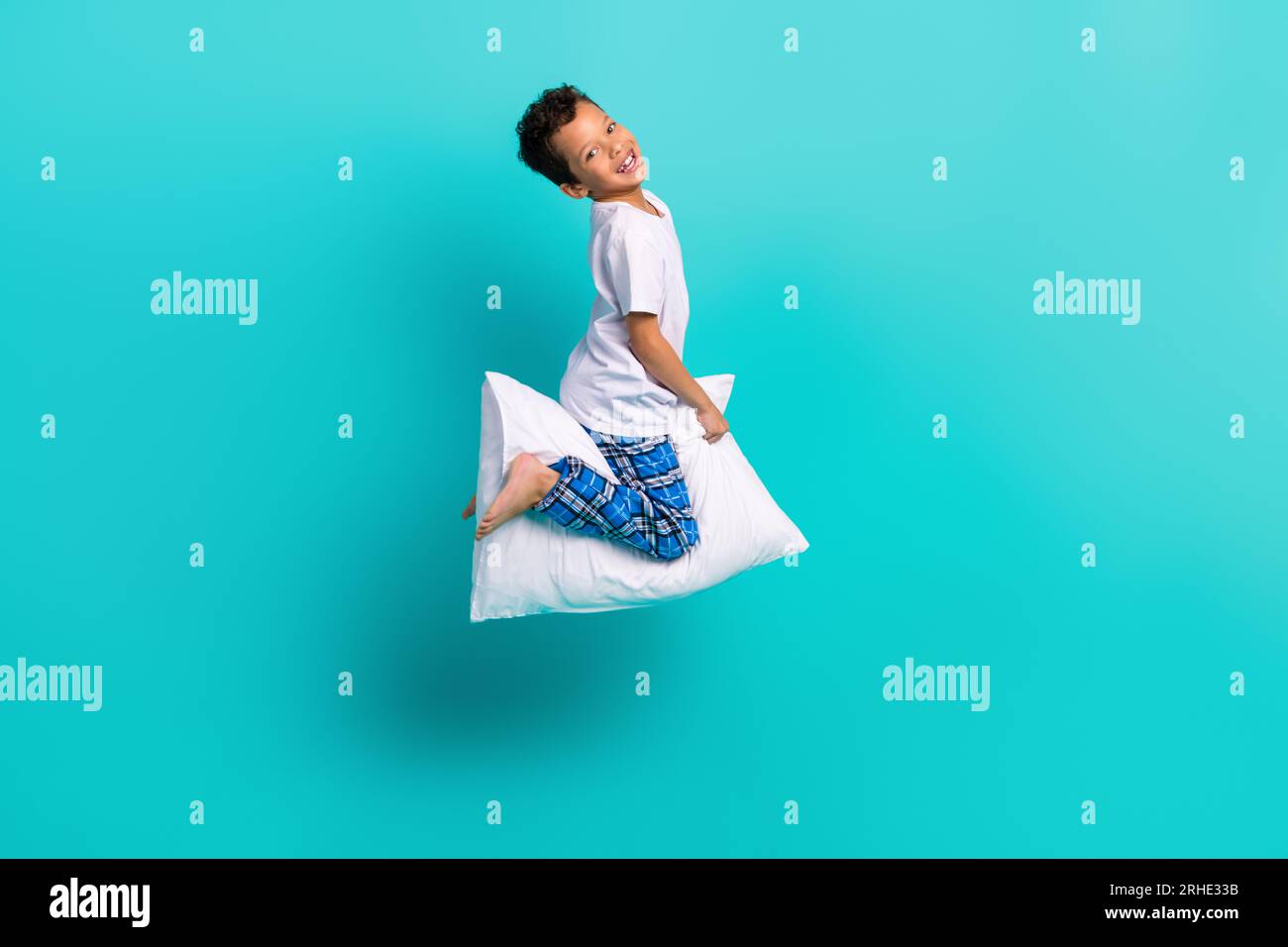 Ganzkörperfoto des kleinen energiegeladenen fröhlichen Jungen, der fliegendes Kissen auf blauem Hintergrund springt Stockfoto