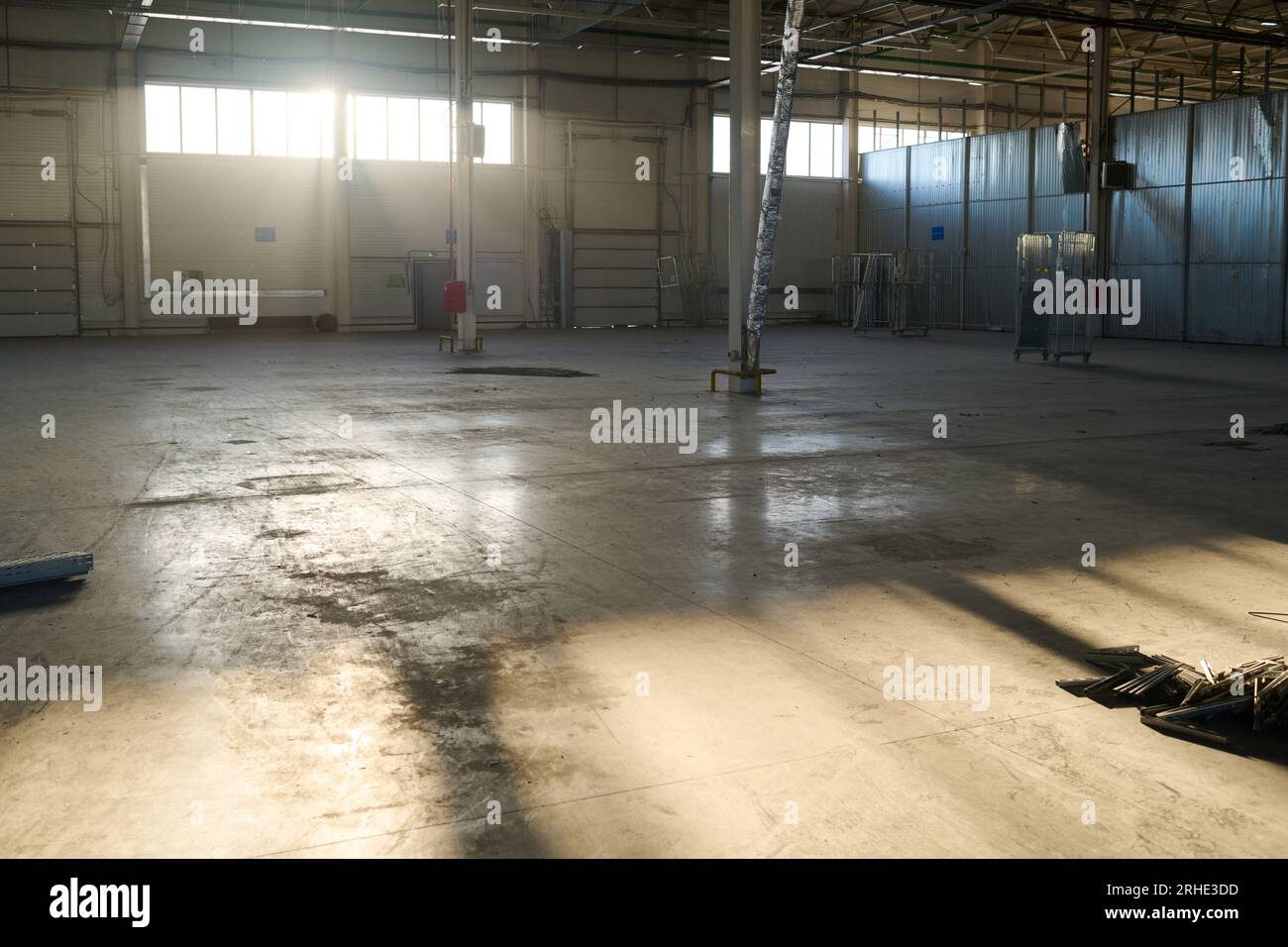 Sonnenbeleuchtete Ecke einer geräumigen Werkstatt oder eines Lagers einer Industrieanlage oder Fabrik mit langen Fenstern und verschiedenen metallischen Konstruktionen Stockfoto