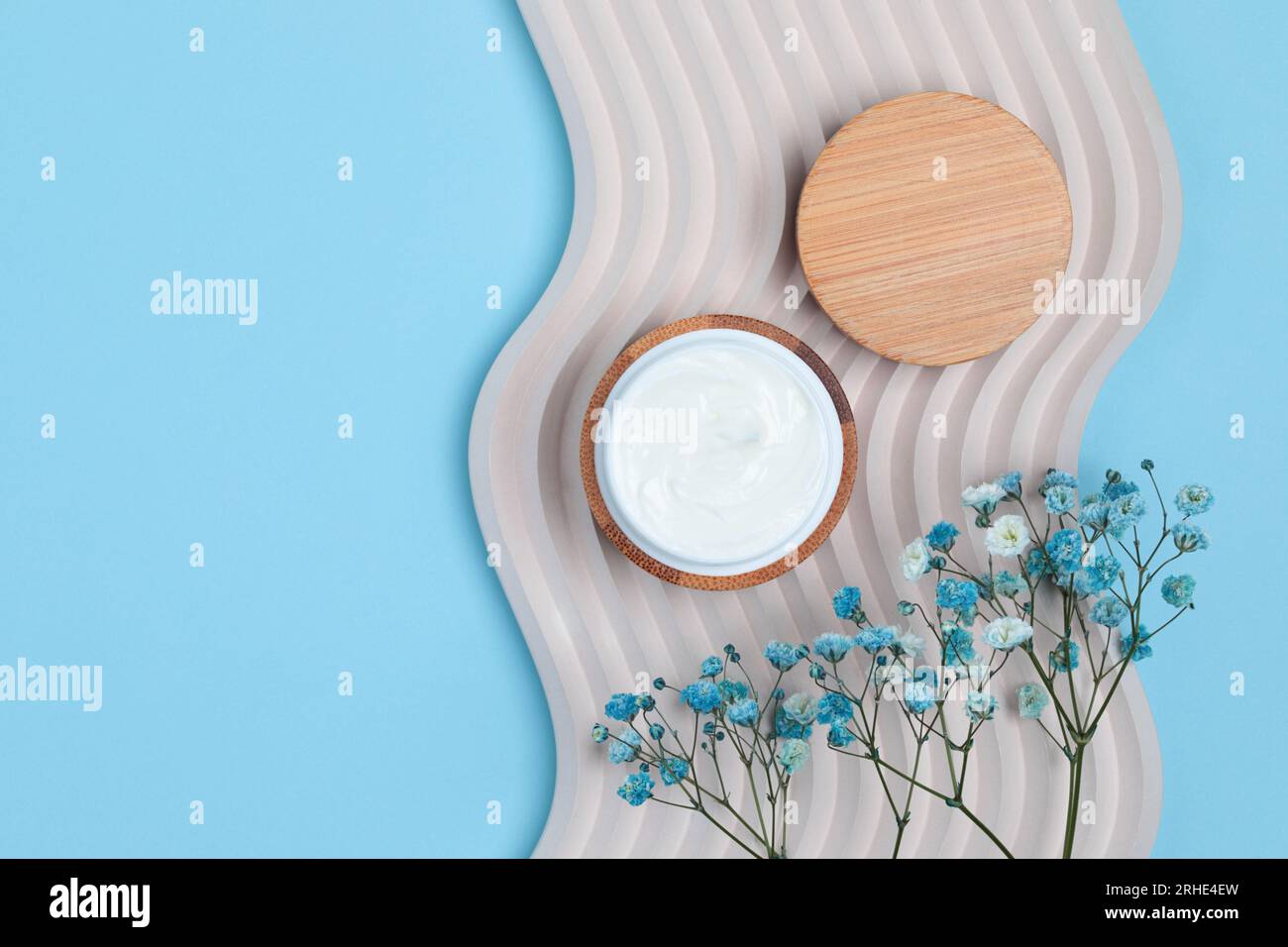 Kosmetische cremefarbene Dose auf Beton Dekorationswelle mit Feldblumen, minimalistisches Design auf blauem Hintergrund, Draufsicht Stockfoto