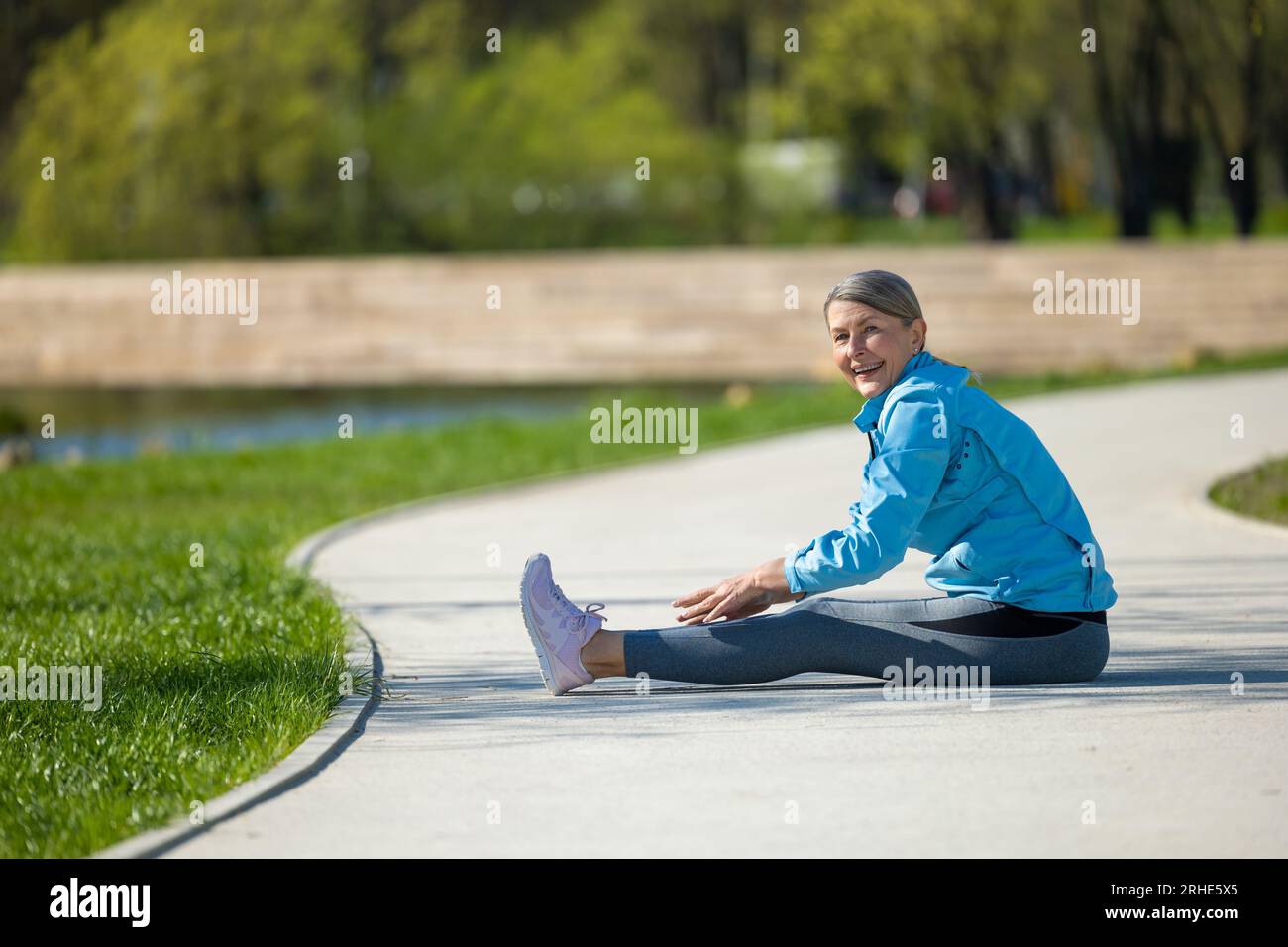 Eine Frau, die im Park auf der Yoga-Matte sitzt und sich streckt Stockfoto