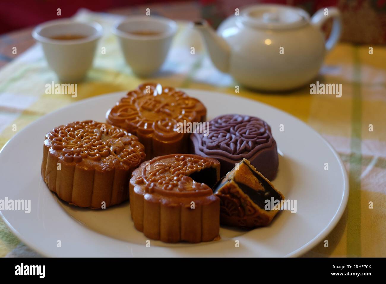 Mitte des Herbstmonds, eine Auswahl von vier chinesischen Mondkuchen auf einem weißen Teller, ein Viertel entfernt mit schwarzem Sesam und rundem Eigelb. Stockfoto