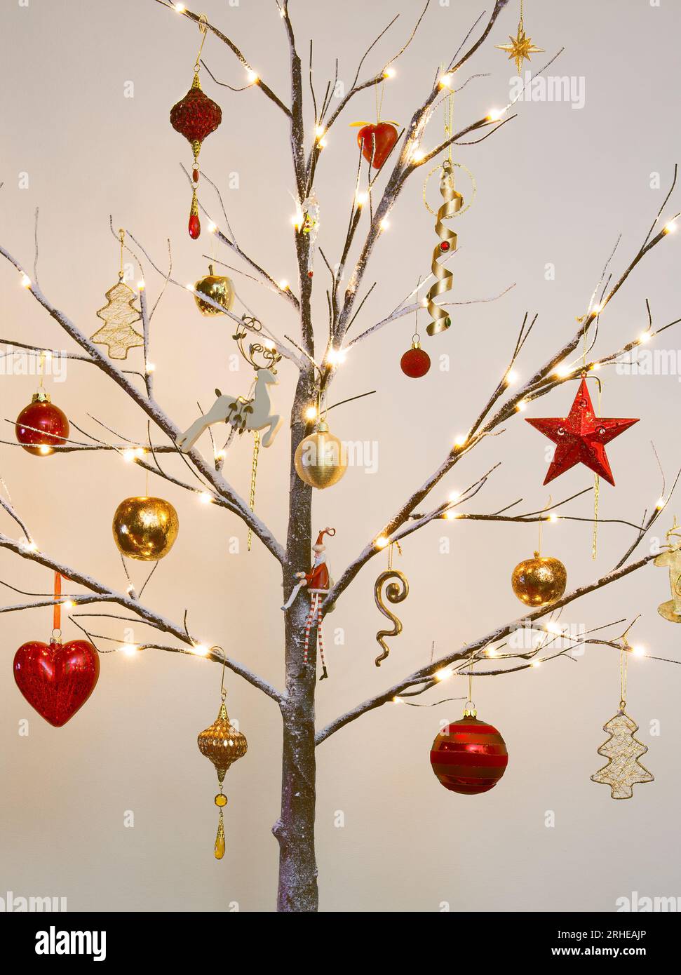 Weihnachtsbaumschmuck in traditionellem Rot und Gold hängt an einem modernen Zweig mit Schnee-Effekt Stockfoto