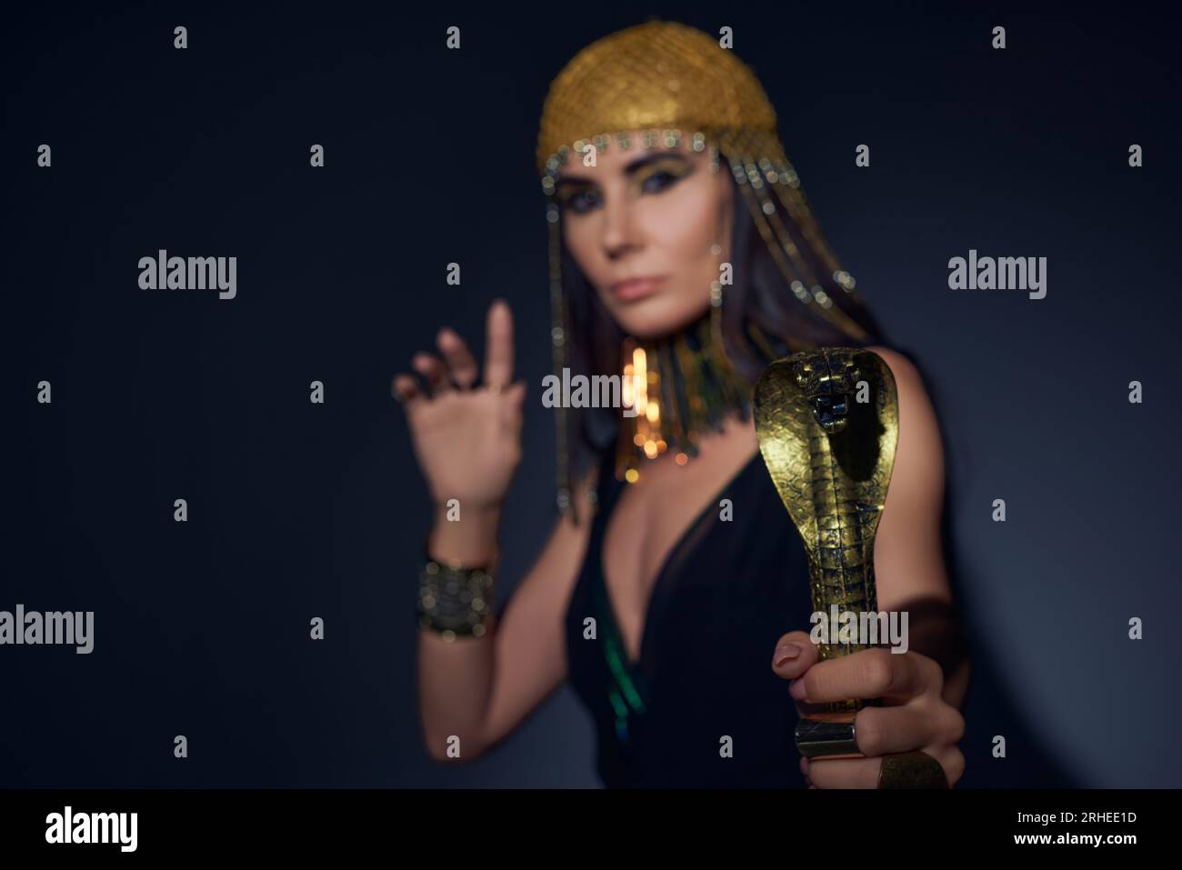 Verschwommene Frau in ägyptischem Look, die einen Gauner in Schlangenform hält und auf blauem Hintergrund steht Stockfoto