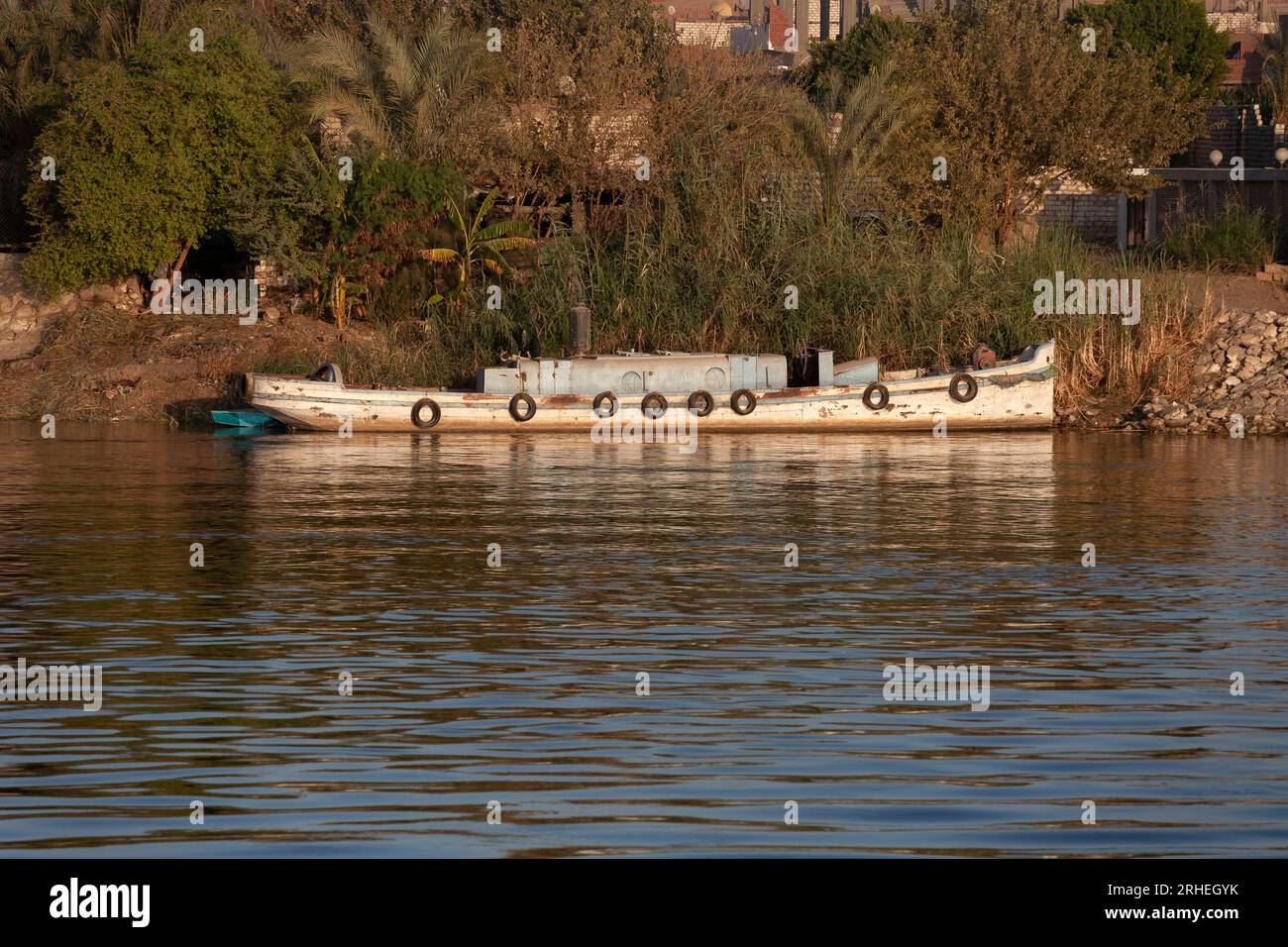 Ein kleines hölzernes Flussboot mit einem einzigen Trichter, das am Ufer des Nils, Ägypten, mit Reflexionen vertäut ist Stockfoto