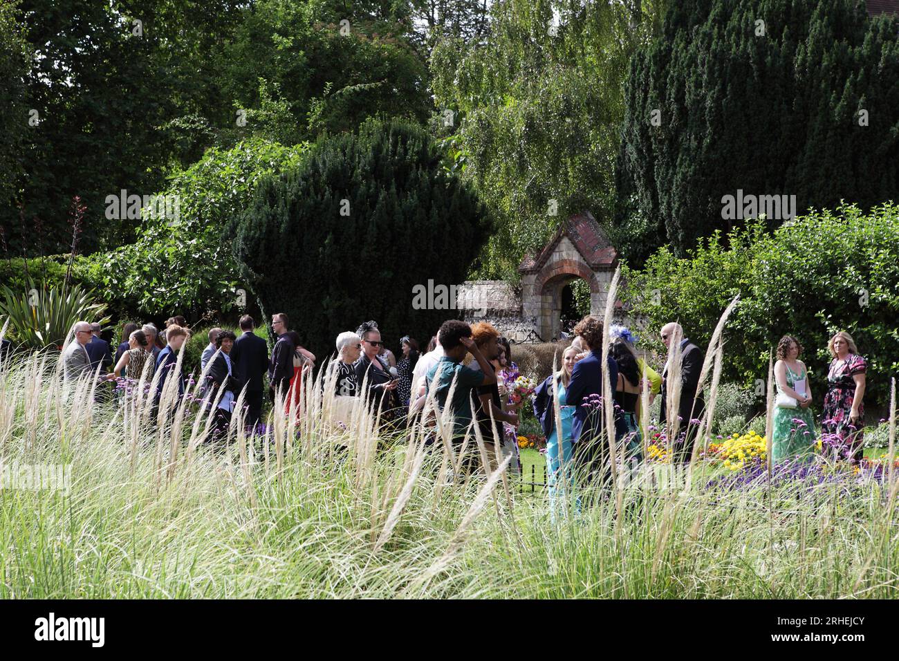 Eine Hochzeitsgesellschaft versammelt sich in Southover Grange Gardens, nachdem sie das Kasse hinter den Eibenbäumen besucht hat. Stockfoto