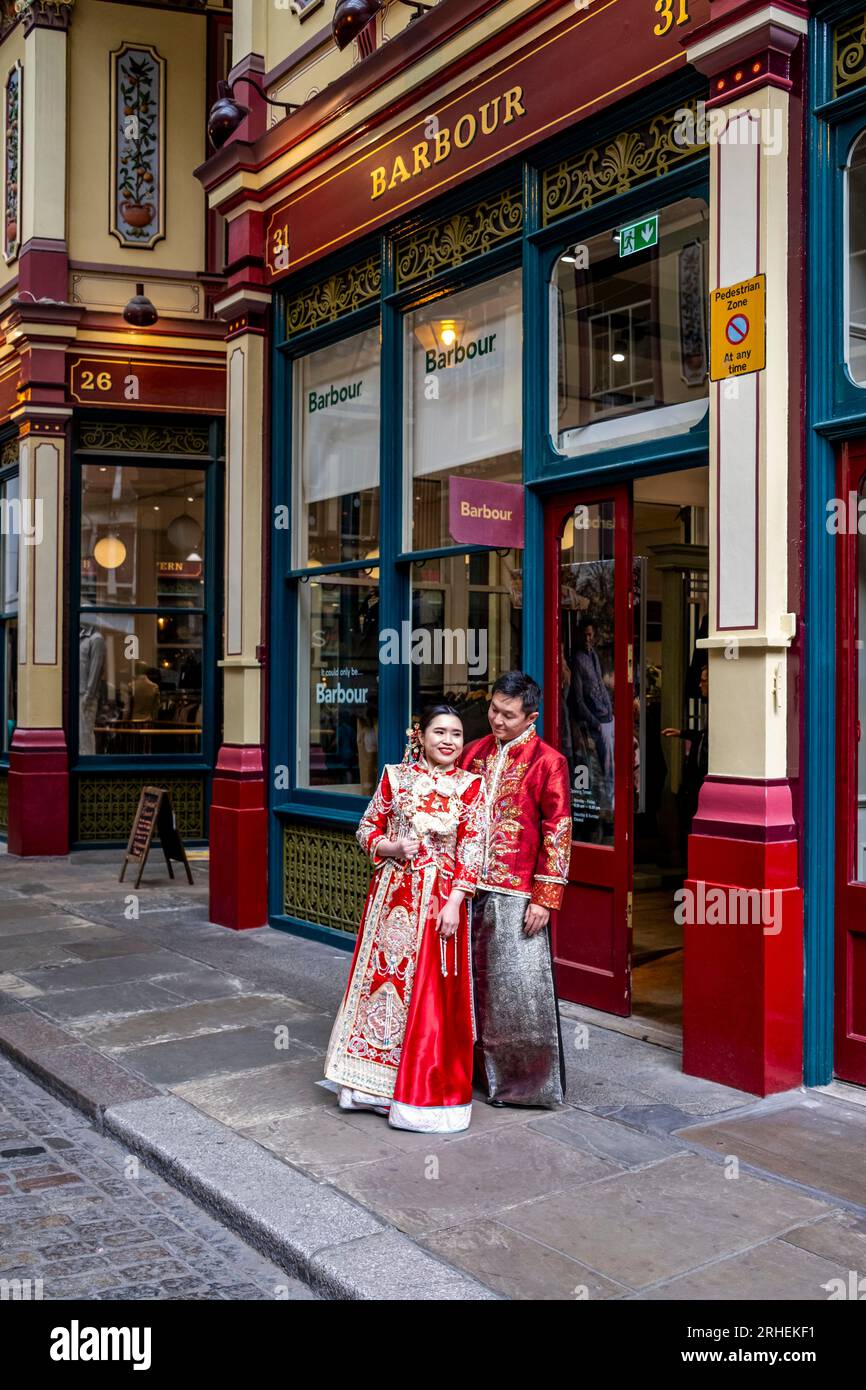Ein chinesisches Paar posiert vor dem Barbour Luxury Clothes Shop in Leadenhall Market, London, Großbritannien, für Hochzeitsfotos in traditionellem Kostüm. Stockfoto