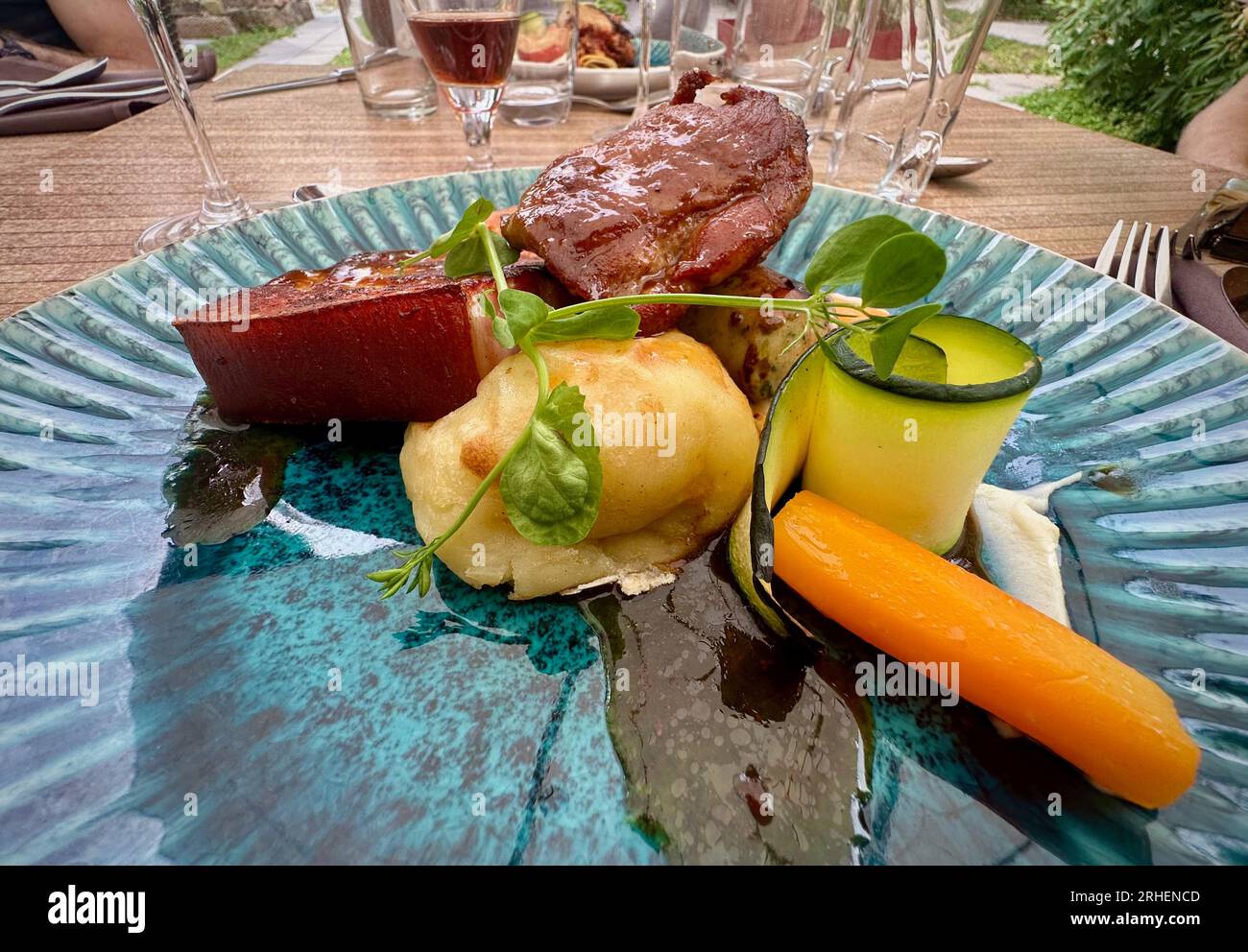 Gastronomischer Genuss: Buntes Schweinefleisch in einem Restaurant, serviert auf einer Blauen Platte mit Wein Stockfoto