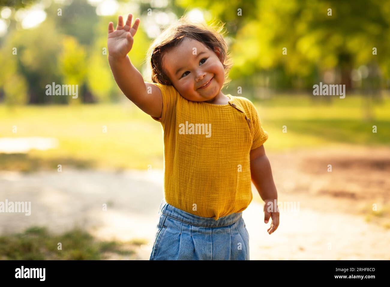 Entzückendes Kleines Mädchen In Lässiger, Winkender Hand, Die Draußen Steht Stockfoto
