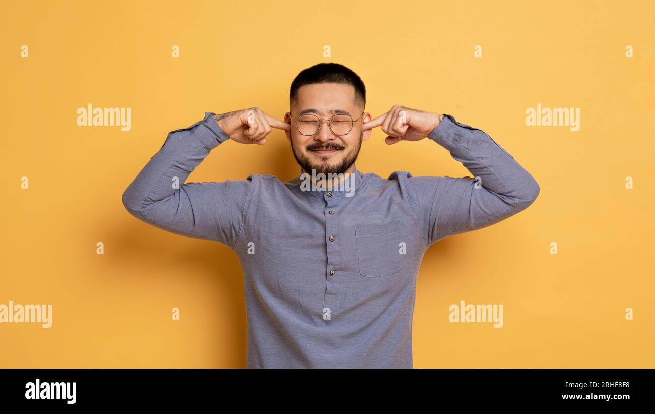 Porträt eines jungen asiatischen Mannes, der Ohren mit Fingern und Stirnrunzeln verstopft Stockfoto