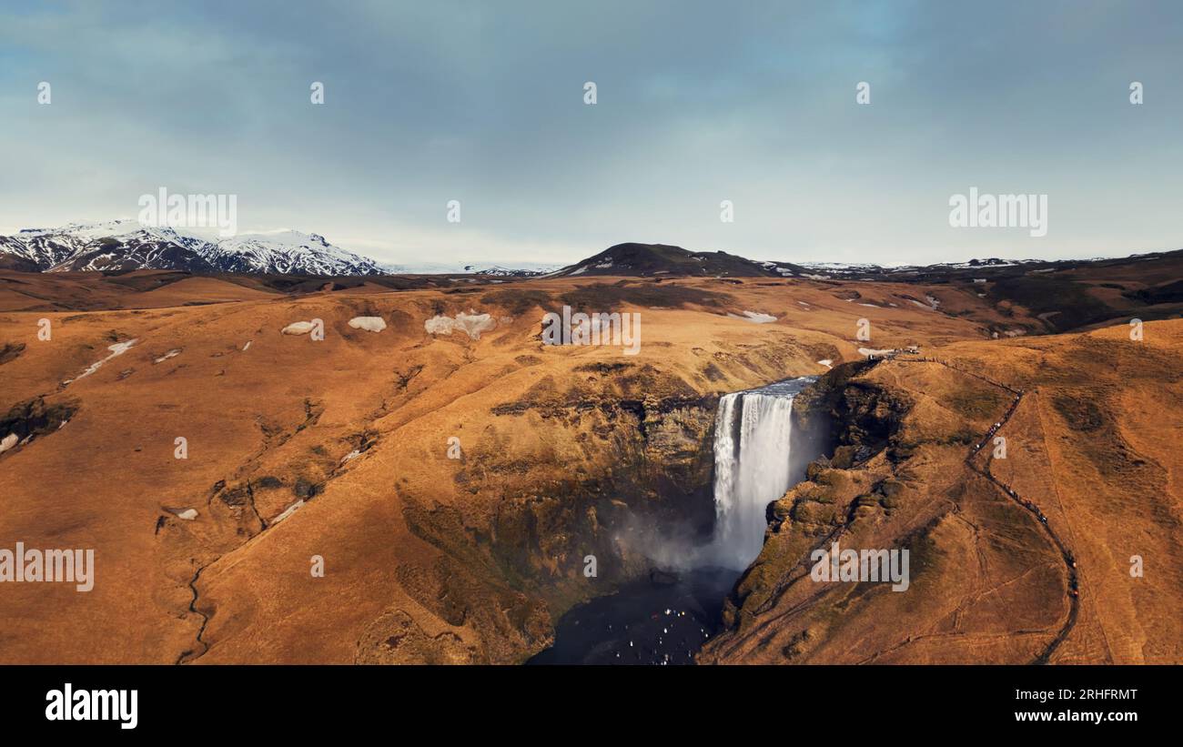 Luftaufnahme der arktischen Skgafoss-Kaskade, die von den gefrorenen Hügeln abfließt und eine spektakuläre isländische Landschaft schafft. Massiver skandinavischer Wasserfall fällt von braunen Klippen. Zeitlupe. Stockfoto