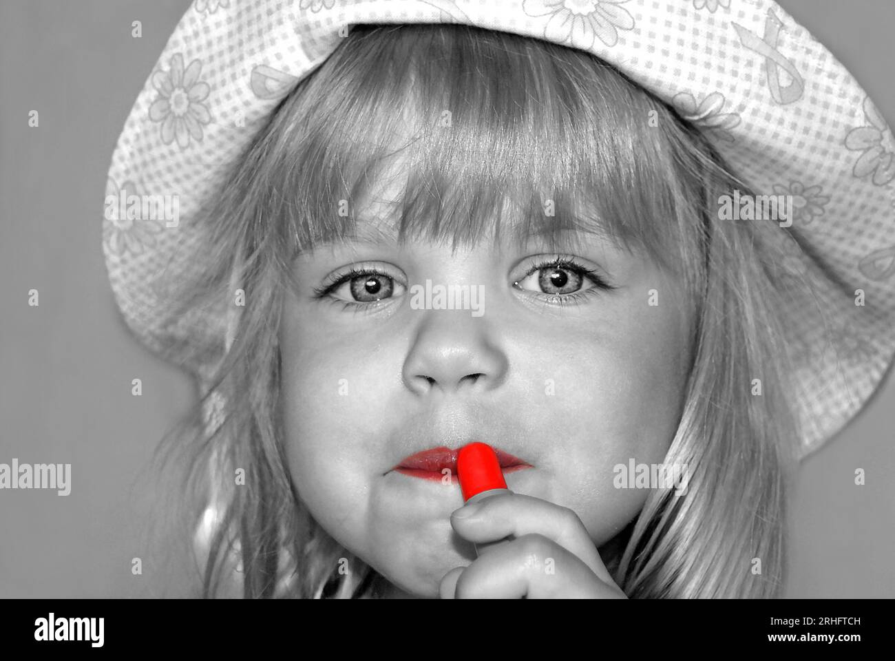 Kleines blondes Mädchen, das den roten Lippenstift in selektiver Farbeffektion abnimmt Stockfoto
