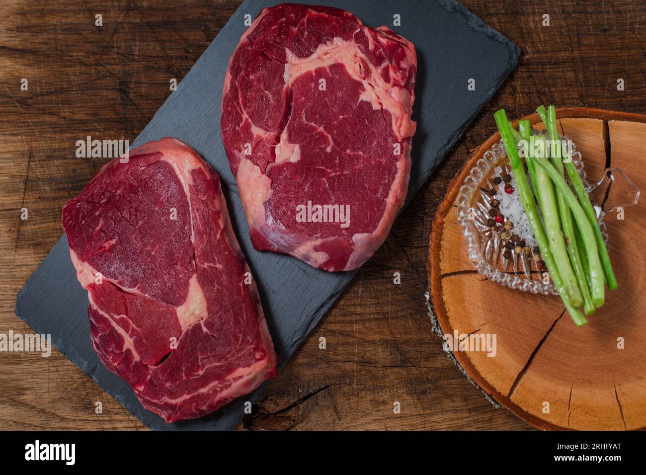 Zwei Ribeye-Steaks mit Salz und Pfeffer auf dem schwarzen Schneidebrett Stockfoto