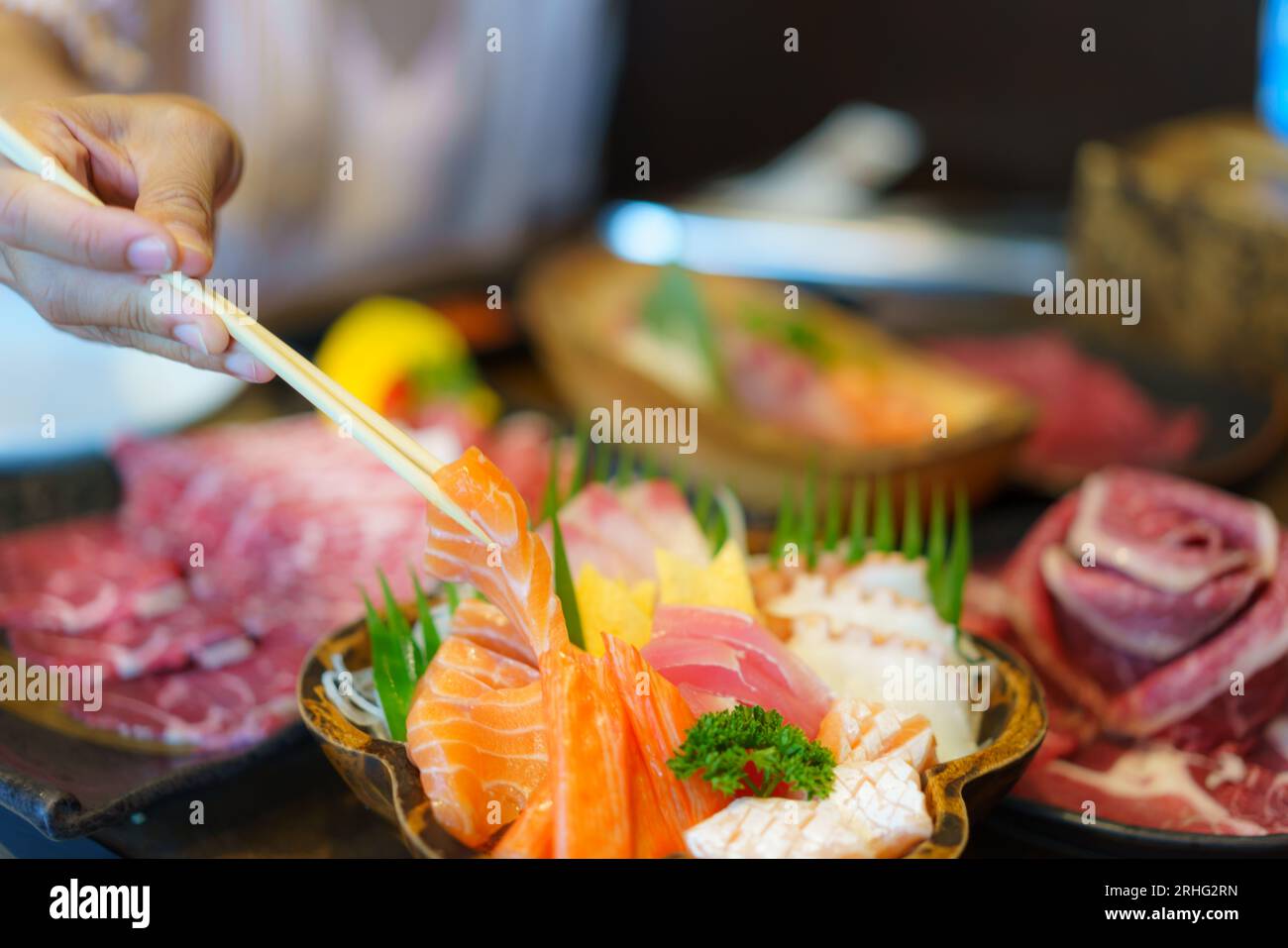 Eine Frau schwingt Stäbchen, um frischen Lachs Sashimi in einem japanischen Restaurant auf einen Teller zu legen und die Kunst des Essens einzufangen. Stockfoto