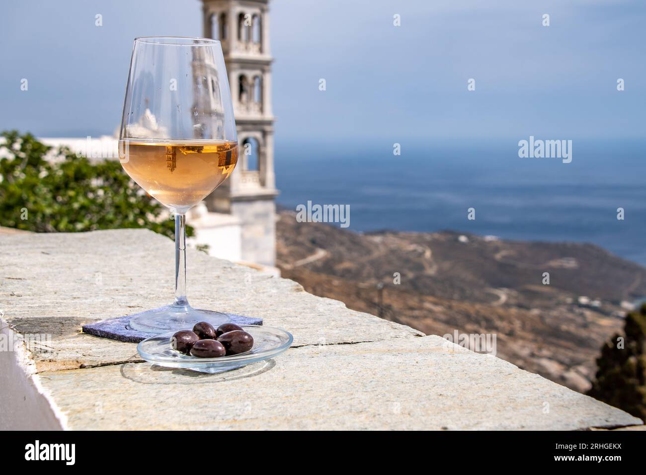 Roséwein auf einem Steinbalkon mit bunten blauen Fensterläden und dem blauen Ägäischen Meer in der Ferne: Tinos Island Griechenland Stockfoto
