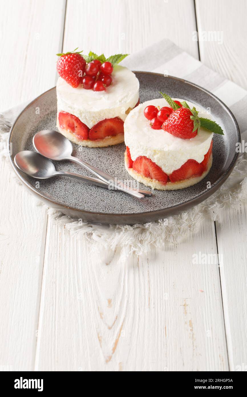 Französischer Mini Cake Fraisier mit frischen Erdbeeren und Johannisbeeren auf dem Teller auf dem Tisch. Vertikal Stockfoto