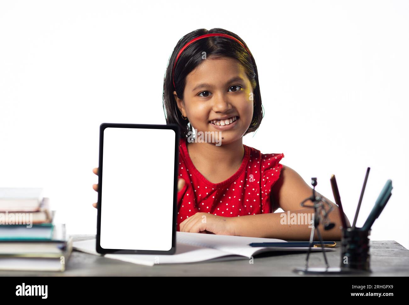 Ein hübsches indisches Mädchen, das studiert und auf dem Tisch auf weißem Hintergrund einen leeren Bildschirm mit Tablet zeigt Stockfoto