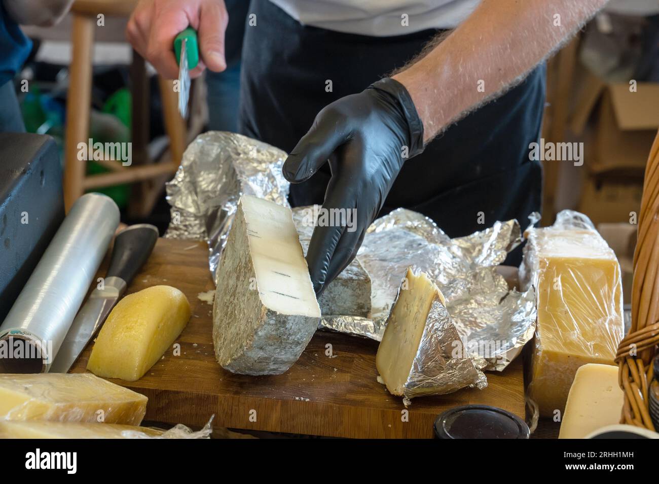 Die Hände des Verkäufers haben ein Stück Käse abgeschnitten. Russischer Bauernkäse vom Hersteller. Auswahl an leckerem Käse auf der Theke. Stockfoto