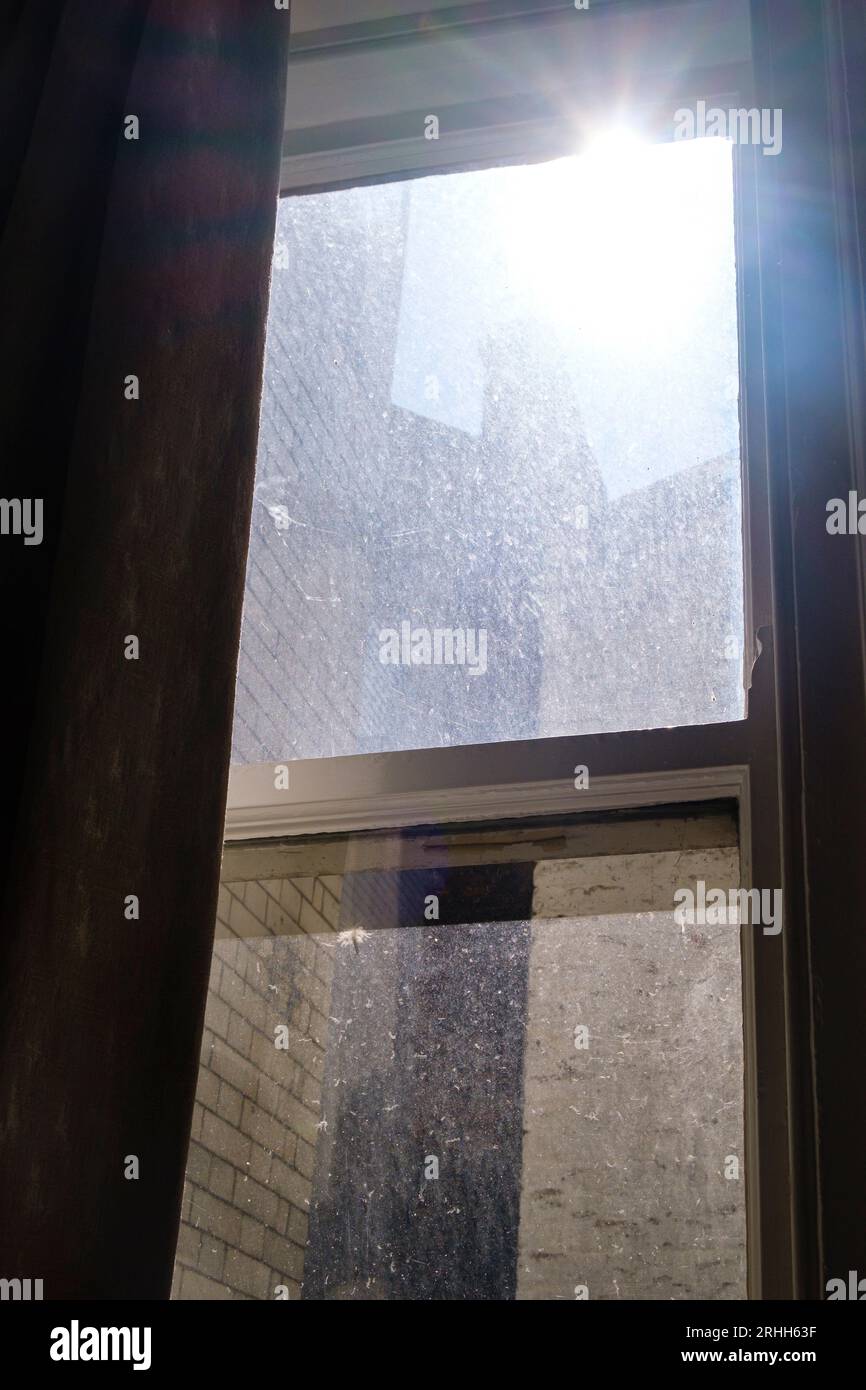 Blick aus einem alten schmutzigen Fenster in einem Apartmentgebäude mit Gebäuden, die die Aussicht versperrten und einem Sonnenstrahl über dem Haus. Stockfoto