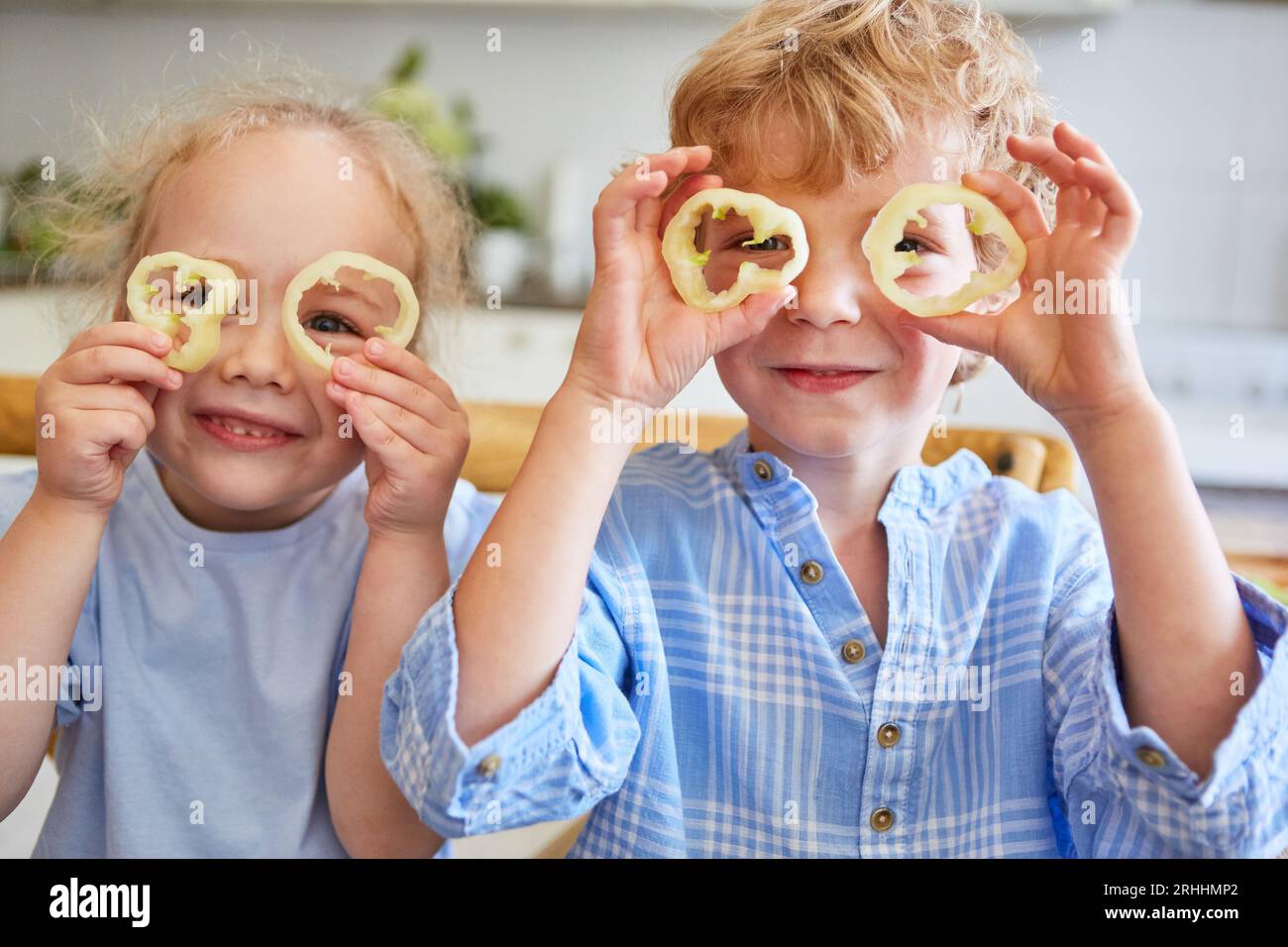 Porträt eines lächelnden Jungen und Mädchens, der beim Spielen zu Hause durch Scheiben von Paprika schaut Stockfoto