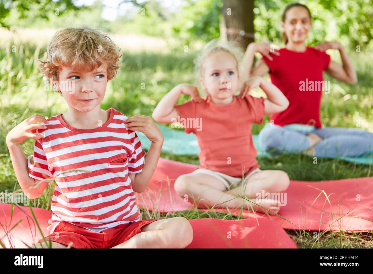 Junge, der Schultertraining macht, während die Familie im Park auf der Matte sitzt Stockfoto