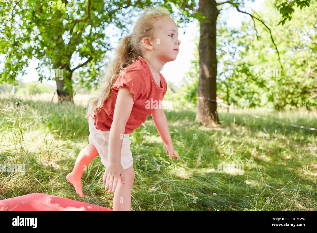 Niedliches Mädchen, das im Garten auf Yogamatte über Gras balanciert Stockfoto