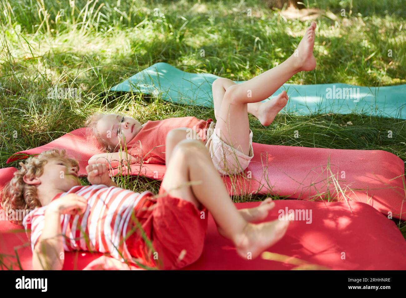 Geschwister genießen miteinander, während sie auf der Yogamatte im Park liegen Stockfoto