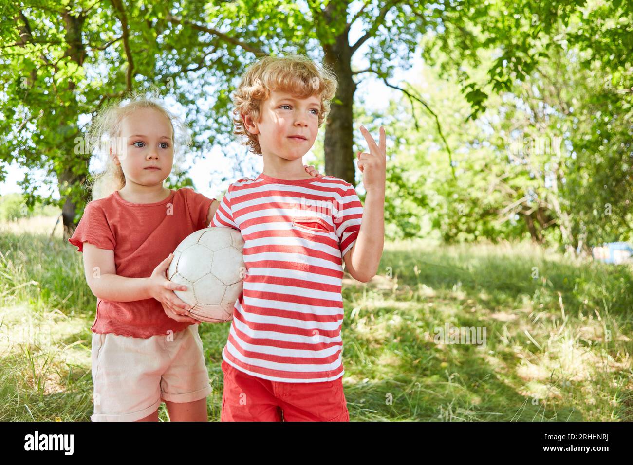 Bruder zeigt Friedenszeichen, während Schwester im Garten Fußball hält Stockfoto