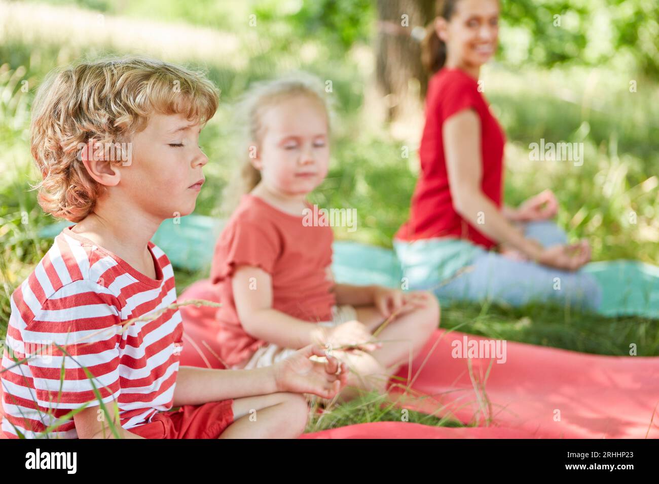 Konzentrierter Junge, der Yoga mit der Familie im Park macht Stockfoto