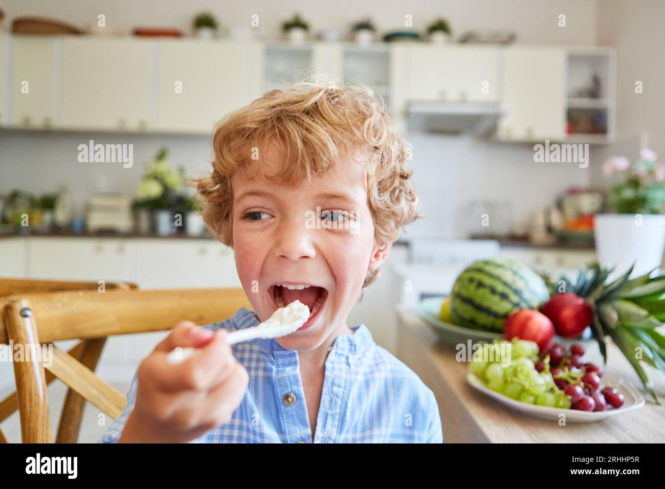 Blonder Junge, der zu Hause in der Küche frischen Joghurtparfait aus dem Löffel isst Stockfoto