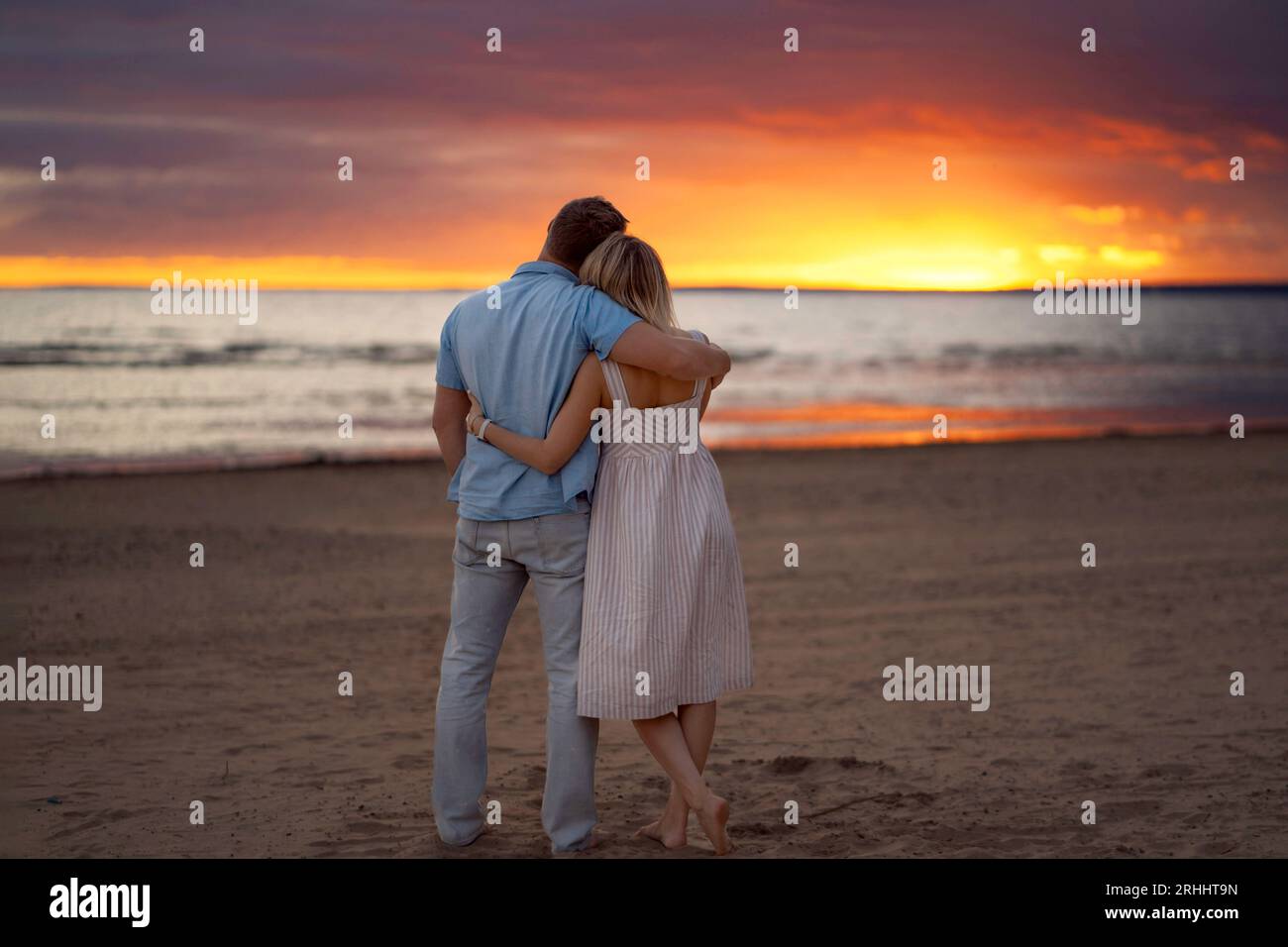 Glückliches Paar, das bei Sonnenuntergang am Strand steht, umarmt und auf das Meer schaut. Wunderschöner violetter und gelber Himmel auf dem Hintergrund. Romantisches Foto für Eltern Stockfoto