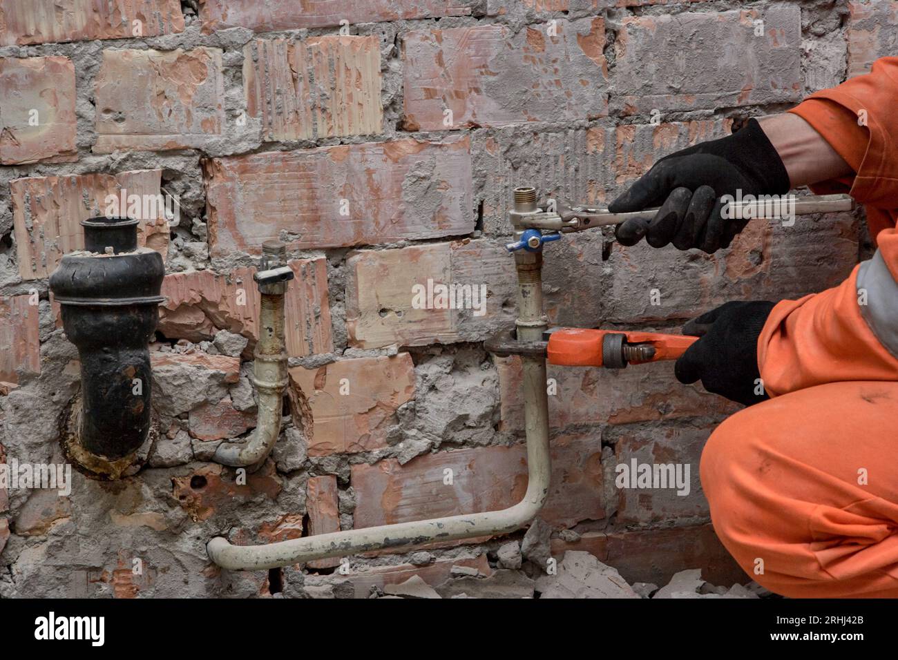 Befestigung des undichten Wasserventils durch den Bauunternehmer mit Handschuhen und orangefarbenen Overalls. Stockfoto