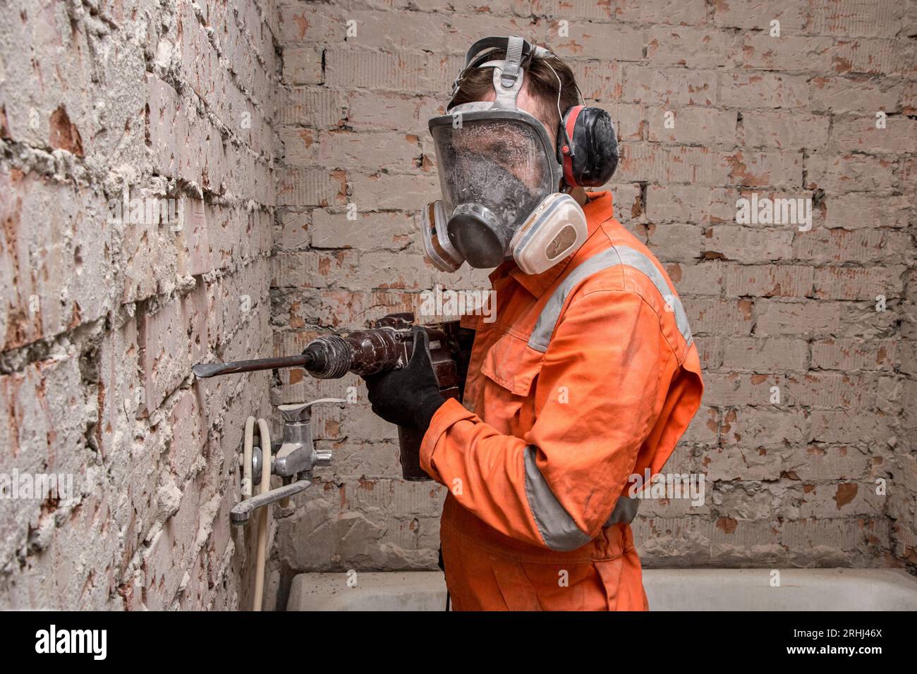 Bauarbeiter, der Vollgesichts-Atemschutzmaske und Gehörschutz für die Arbeit mit einem Bohrhammer trägt. Stockfoto