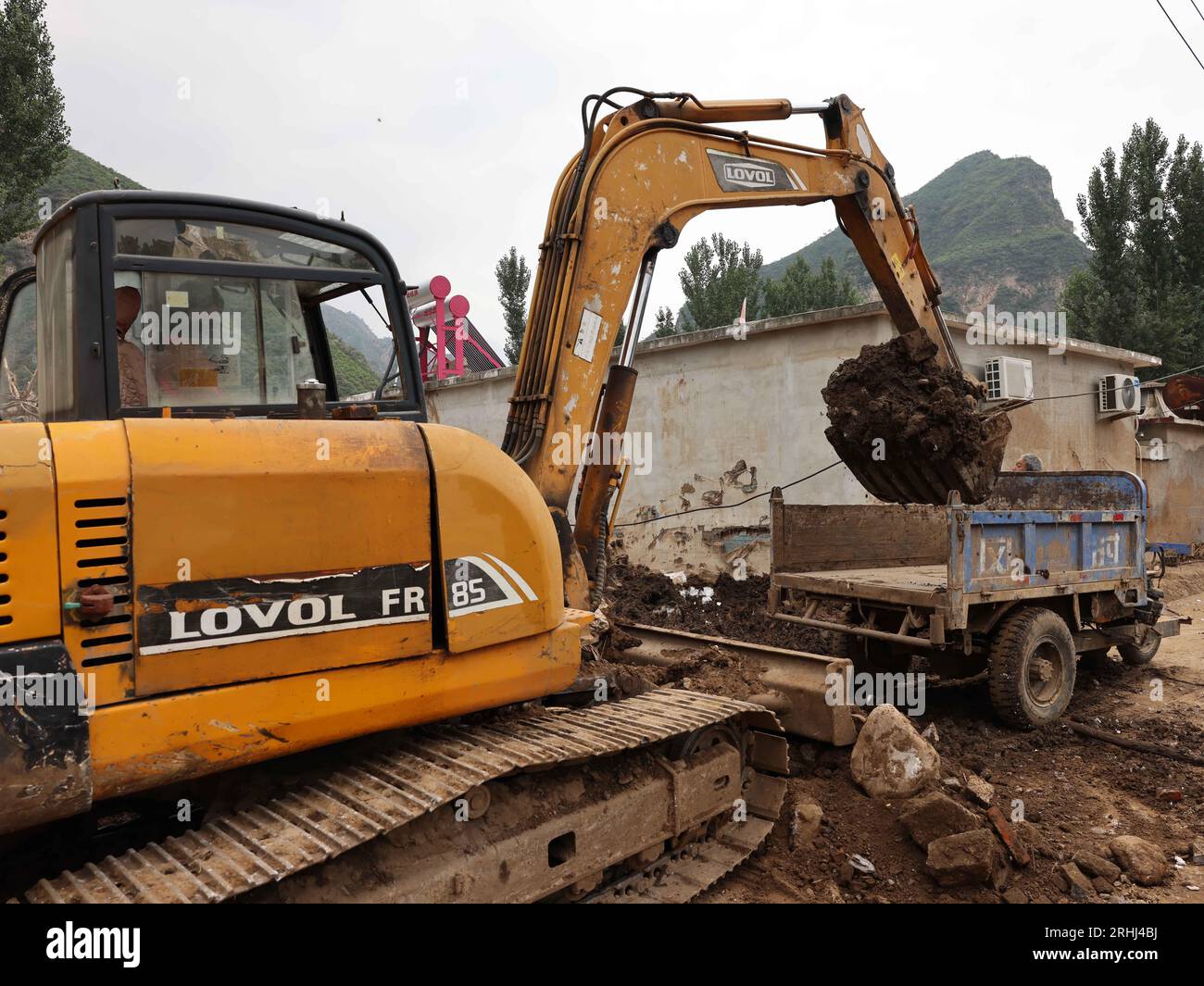 Baoding, chinesische Provinz Hebei. Aug. 2023. Ein Arbeiter fährt einen Bagger, um Schlamm im Dorf Pingyu im Laishui County in der nordchinesischen Provinz Hebei am 17. August 2023 aufzuräumen. Laishui County hat durch die Auswirkungen des Taifuns Doksuri in letzter Zeit starke Niederschläge erlitten. Die lokalen Behörden haben aktiv den Wiederaufbau nach Katastrophen durchgeführt, um die Sicherheit der Bewohner zu gewährleisten und den von Überschwemmungen betroffenen Regionen wieder auf Kurs zu bringen. Quelle: Luo Xuefeng/Xinhua/Alamy Live News Stockfoto