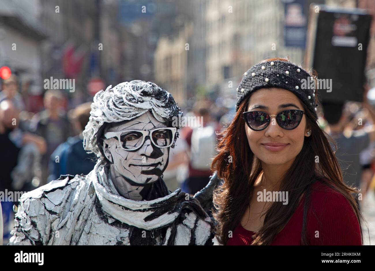 Royal Mile, Edinburgh, Schottland, Großbritannien. 17. August 2023. In dieser zweiten Woche des Edinburgh Festival Fringe war es ein farbenfroher Tag auf der High Street, an dem die verschiedenen Acts ihre Shows und die feurigen Straßenkünstler bewerben. Im Bild: Ein Tourist posiert für ein Foto mit der Statue von Human Living Estevan Mortensen. Credit/Archwhite/Alamy Live News. Stockfoto