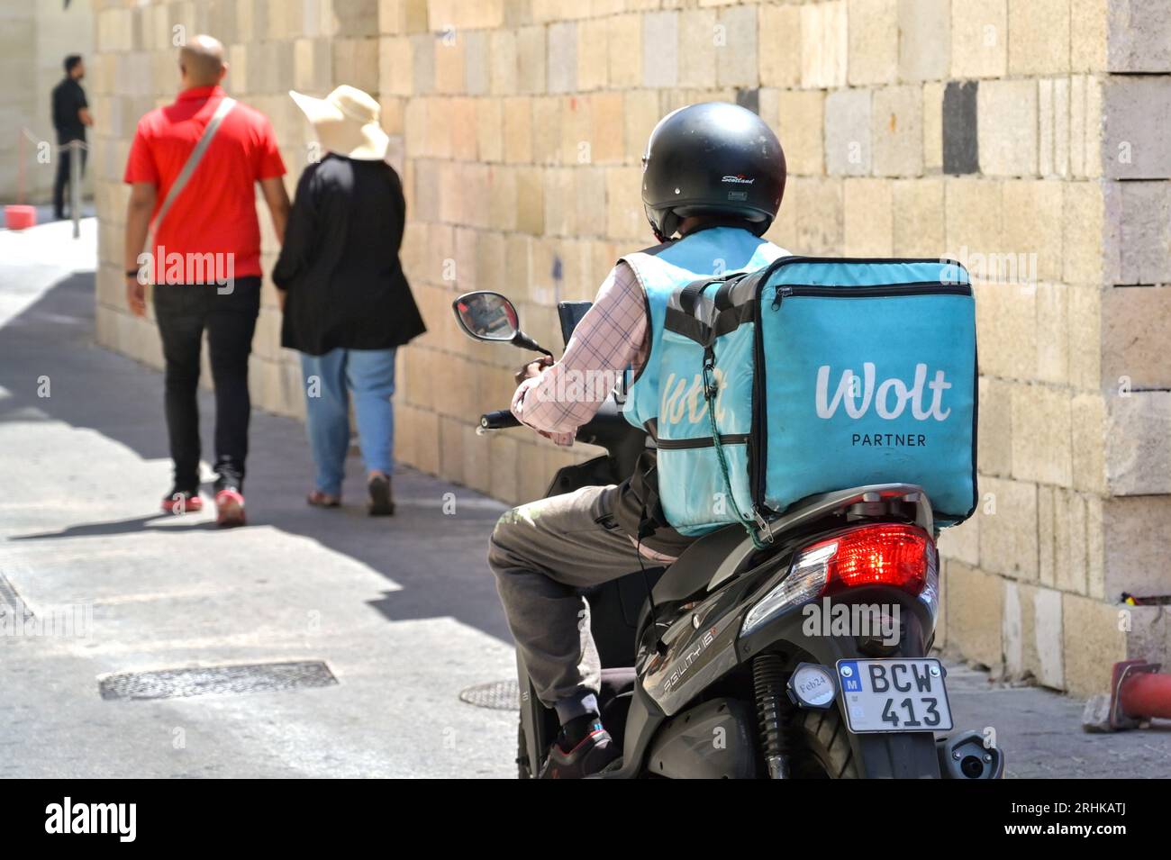 St Julians, Malta - 6. August 2023: Person, die einen Motorroller mit einem isolierten Container für den Wolt Food Take Way auf der Rückseite fährt Stockfoto