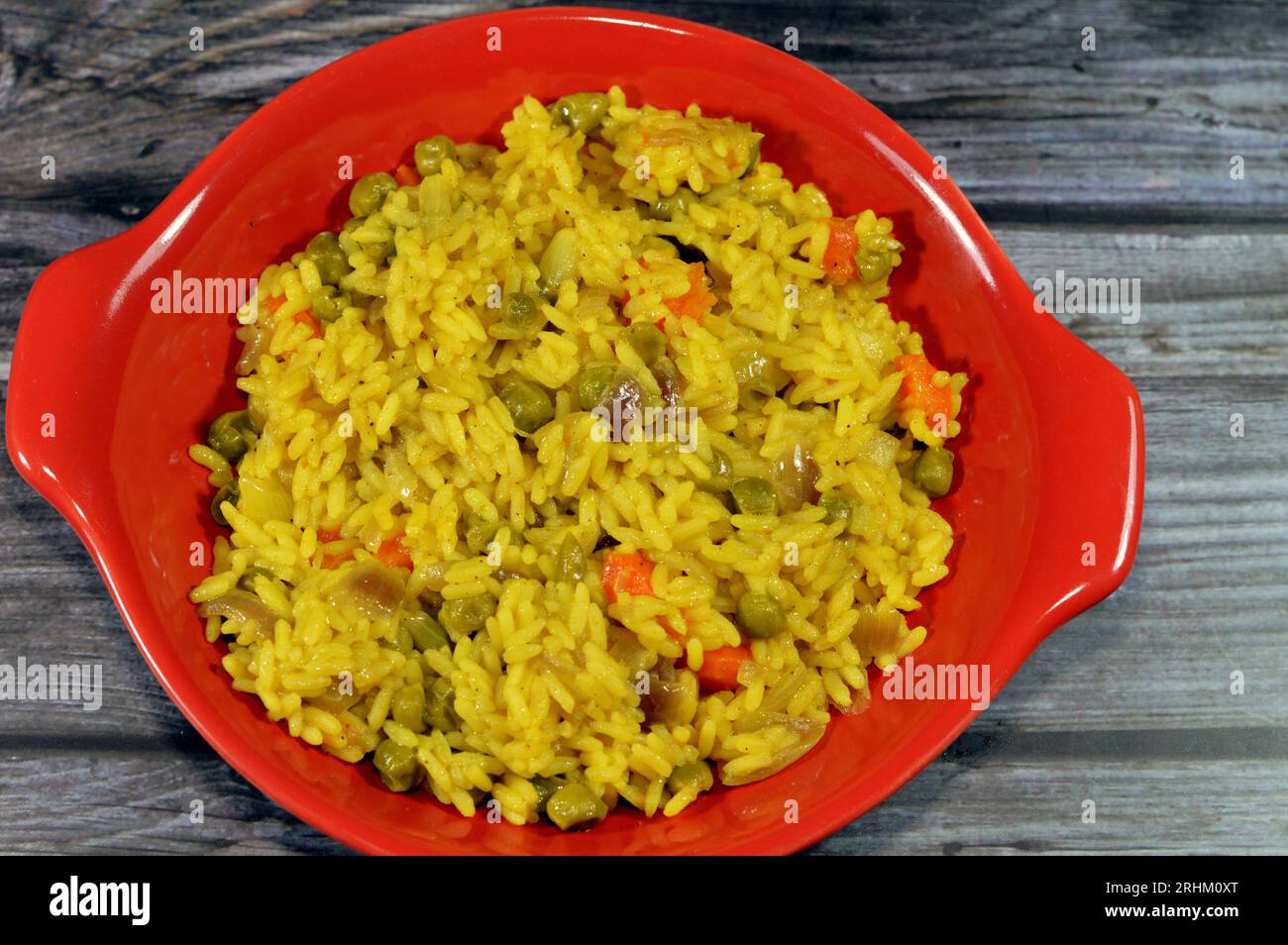 Ein Teller mit heiß gedämpftem langkornigen gelben Basmati-Reis mit Gemüseerbsen und Karotten mit geschnittenen Zwiebeln, chinesische Küche Rezept und auch von orientalisch Stockfoto