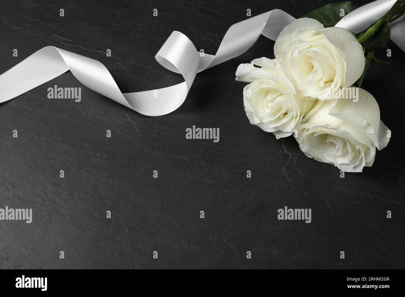 Weiße Rosen und Band auf schwarzem Tisch, Platz für Text. Beerdigungssymbole Stockfoto