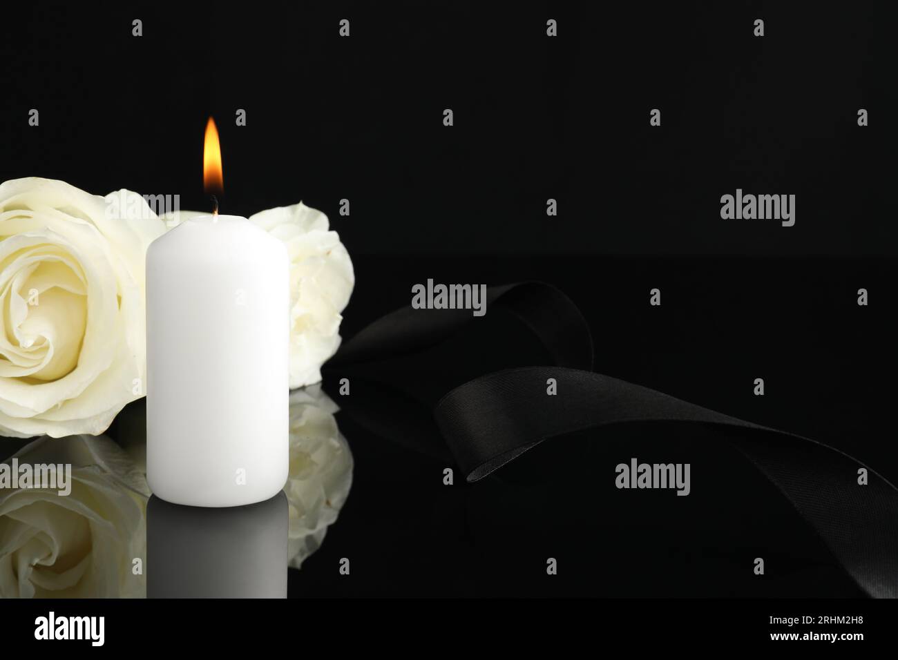 Brennende Kerze, weiße Rosen und Band auf schwarzer Spiegeloberfläche bei Dunkelheit, Nahaufnahme mit Platz für Text. Begräbnissymbole Stockfoto