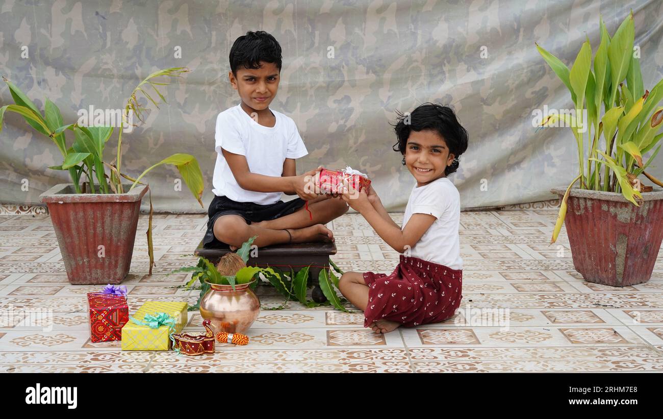 Kleine indische Schwester, die Rakhi an das Handgelenk ihres kleinen Bruders bindet und Geschenke und Süßigkeiten auf dem Raksha Bandhan oder Bhai Dooj Festival austauscht Stockfoto