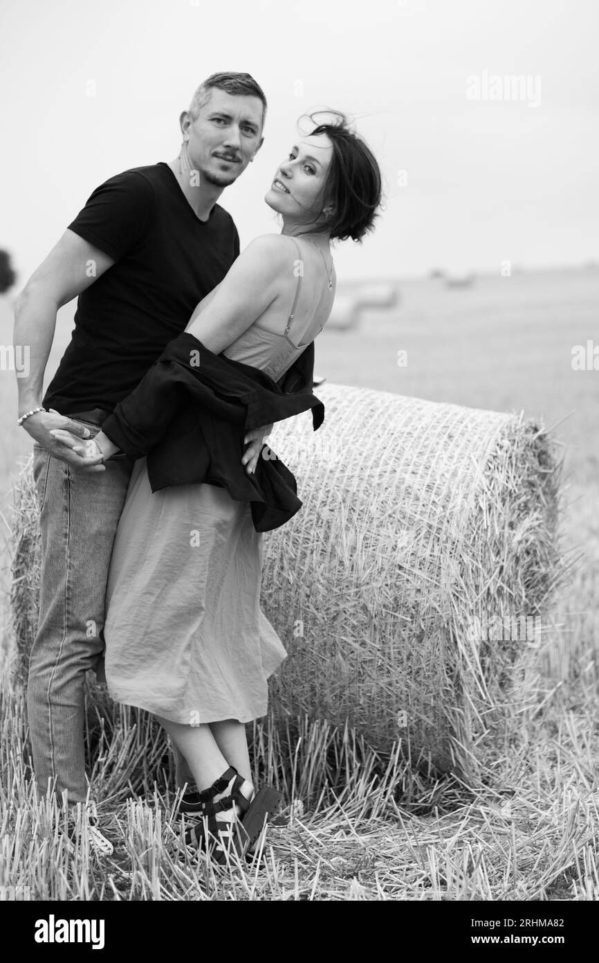 Ein junges Paar wunderschöner Leute hat Spaß auf dem Feld in der Nähe von runden Heuballen. Ein Mann, der mit seiner Frau in der Nähe eines Strohballens tanzt. Schwarz und weiß Stockfoto
