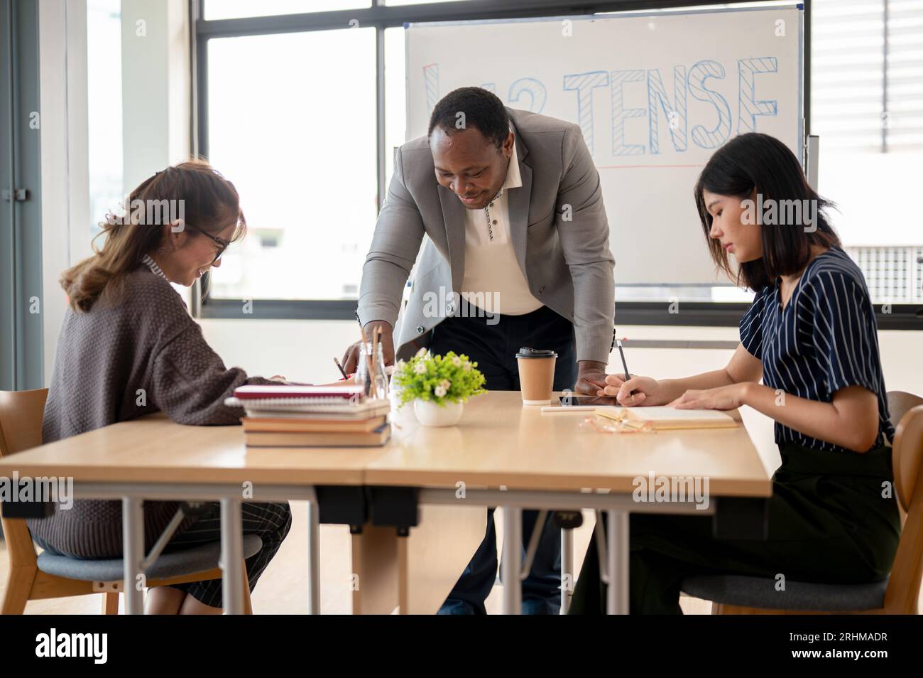Ein professioneller Afro-amerikanischer Englischlehrer unterrichtet asiatische Schüler im Klassenzimmer an einer Sprachschule. Bildungskonzept Stockfoto