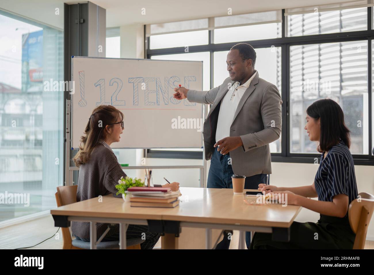 Ein professioneller afroamerikanischer englischer Lehrer oder Tutor, der eine Frage von seinen asiatischen Schülern stellt, während er Englisch unterrichtet oder unterrichtet. L Stockfoto