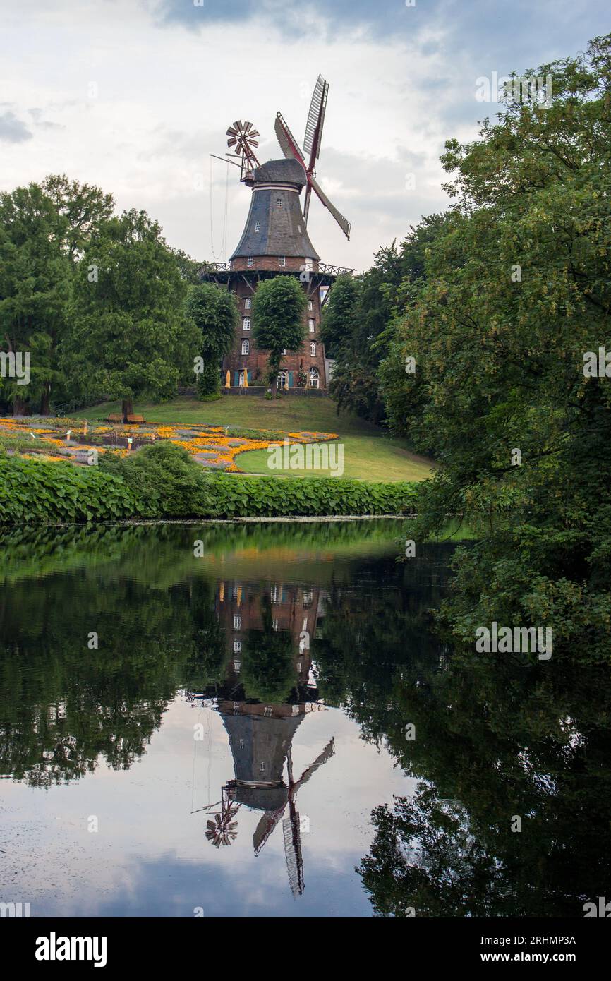 Am Wall Windmühle im Sommerpark mit Teich. Windmühle mit Wasserspiegelung im Stadtgarten. Historische Architektur in Bremen. Landwirtschaftliches deutsches Wahrzeichen. Stockfoto