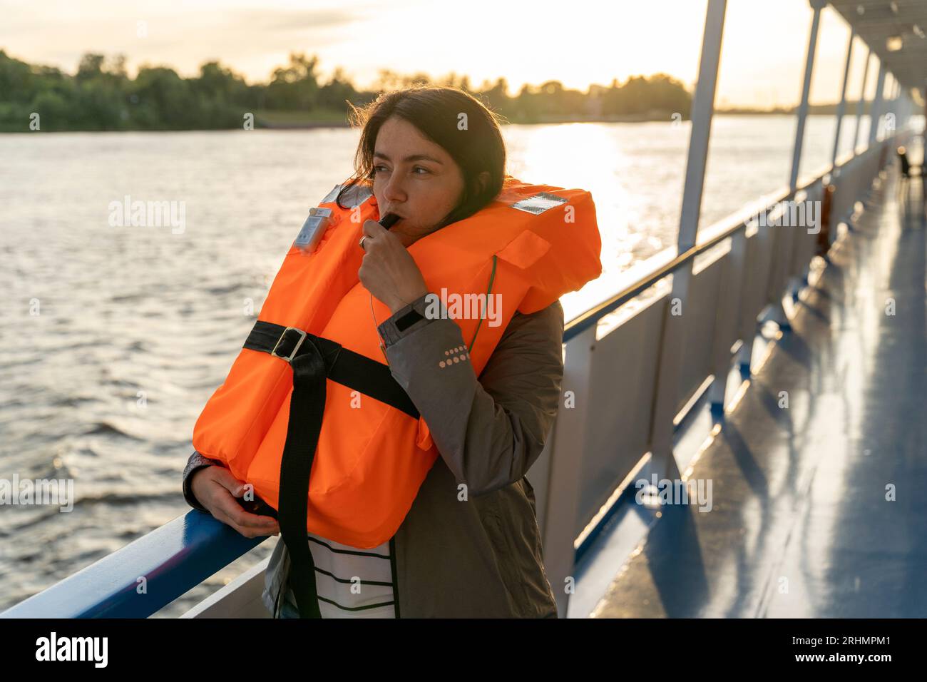 Eine Frau mittleren Alters in einer marineblauen, orangen Schwimmweste schlägt eine Pfeife. Das Mädchen gibt ein Gefahrensignal oder gibt ein Kommando mit einer Pfeife. Eine Übung. Sicherheit Stockfoto