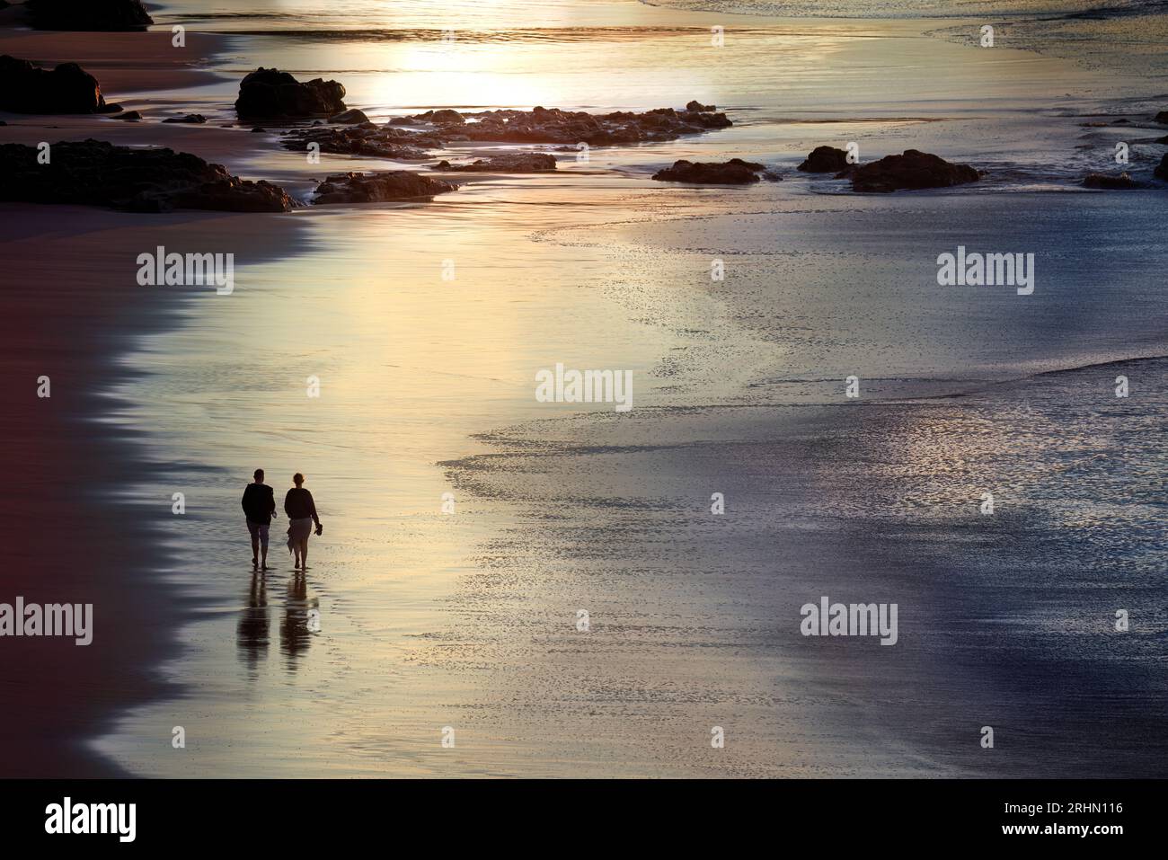 Ein Paar mittleren Alters, das am Abend barfuß am Strand spaziert Stockfoto