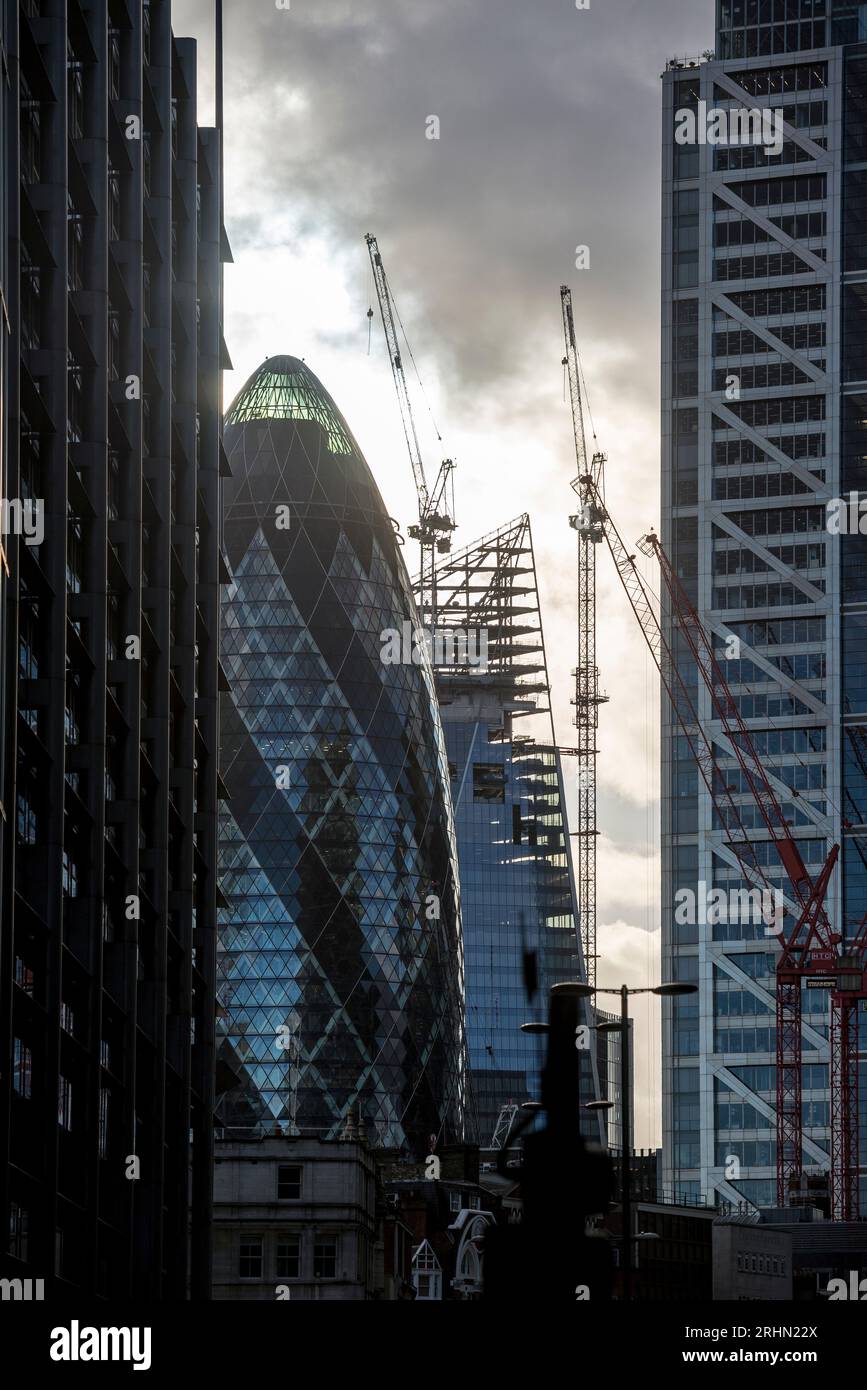 Wolkenkratzer und Kräne in der City of London, einschließlich Gherkin und Scalpel, die in der Abenddämmerung mit stimmungsvollem Himmel umrahmt werden Stockfoto